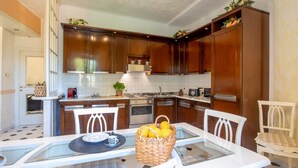 Una cocina moderna con armarios de madera, una isla central y una zona de comedor con sillas blancas y una mesa de vidrio.