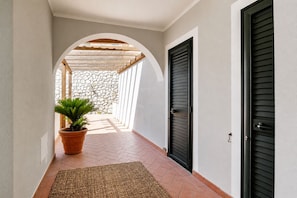 A corridor with a stone wall, a wooden pergola, a potted plant, and a black door. - Casa Andreale, Capoliveri, Centro (Capoliveri)