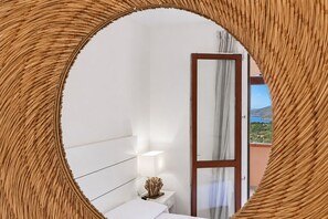 Een slaapkamer met een bed, nachtkastje, lamp en uitzicht op een balkon met een deur.