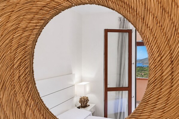 A bedroom with a bed, bedside table, lamp, and a view of a balcony with a door. - Casa Andreale, Capoliveri, Centro (Capoliveri)