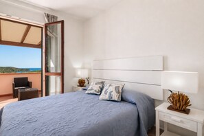 Een slaapkamer met een bed, nachtkastjes, een lamp en uitzicht op het omliggende landschap.