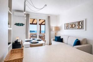 Une pièce comprenant une table à manger dressée pour quatre personnes, un canapé avec des coussins bleus, une lampe et une œuvre d’art accrochée au mur.