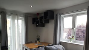 Ein modernes Wohnzimmer mit einem grauen Sofa, einem Holzesstisch und einem Fenster mit Blick auf Bäume.