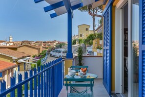 A balcony with a view of a town, a table with cups and a bowl, and a white car parked in the background. - Galatea - Bel Horizonte (Capoliveri)
