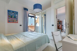 A bedroom with a bed, a desk, and a chair. There is a window with curtains, a painting on the wall, and a door leading to another room. - Galatea - Bel Horizonte (Capoliveri)