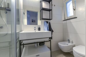 A modern bathroom with a glass shower enclosure, a white sink with a black frame, a bidet, and a small window. - Galatea - Bel Horizonte (Capoliveri)