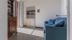 Un soggiorno con un divano blu, un mobiletto in legno e un angolo cottura con scaffali e pensili.