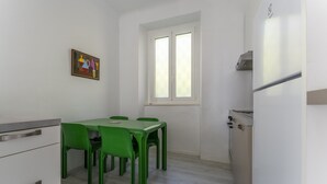 Una cucina compatta con zona pranzo, pareti bianche e una finestra con vetro smerigliato.