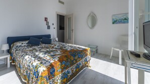 Una camera da letto con un letto grande, una scrivania con un computer, una sedia, uno specchio e una porta che dà su un'altra stanza.