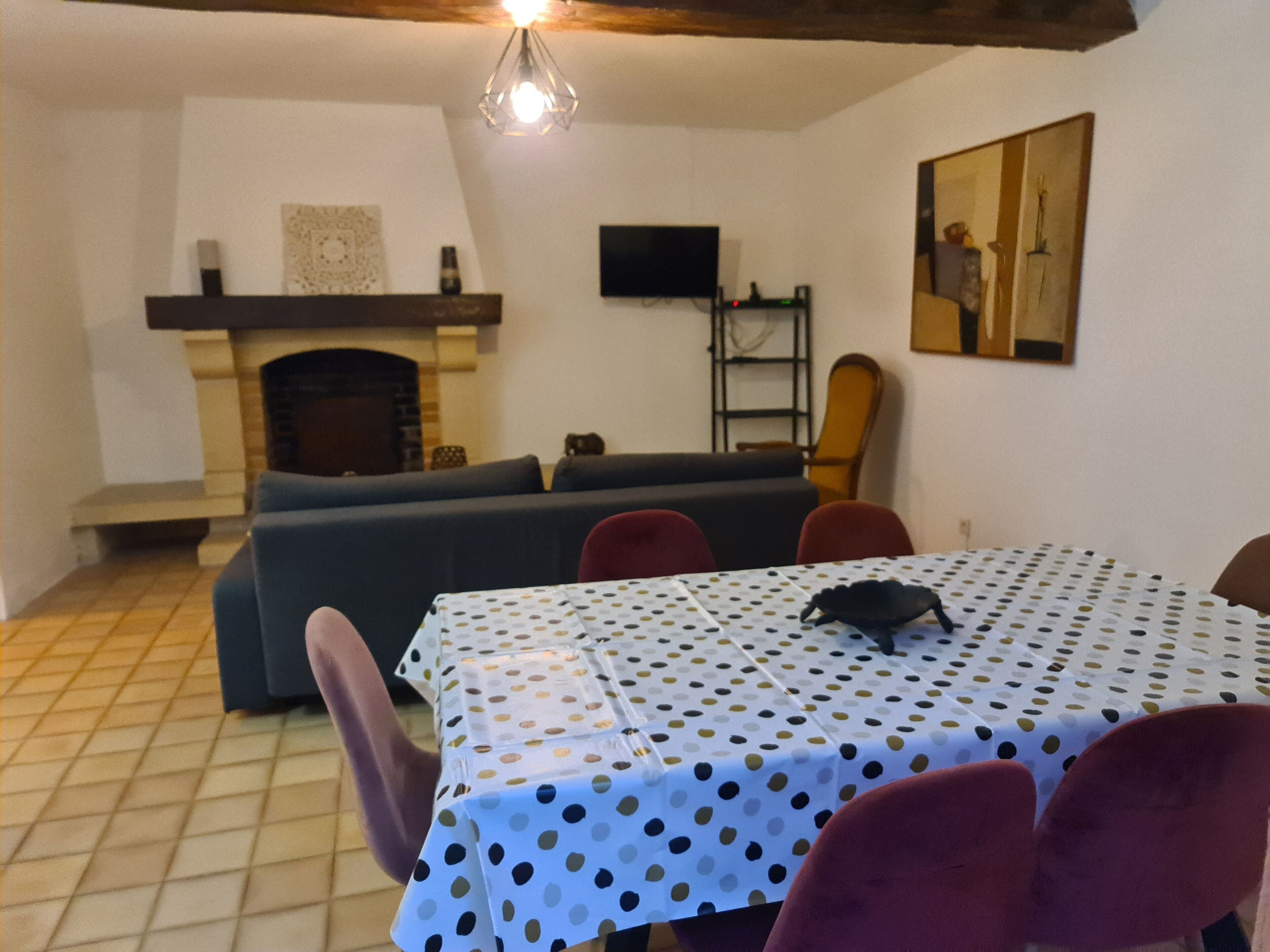 Een woonkamer met een bank, een eettafel met een tafelkleed met stippen, en een open haard.