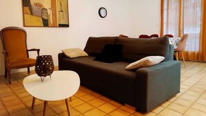 Ein Wohnzimmer mit einer Couch, einem Sessel, einem kleinen Tisch, einer Uhr und einem Bild an der Wand.