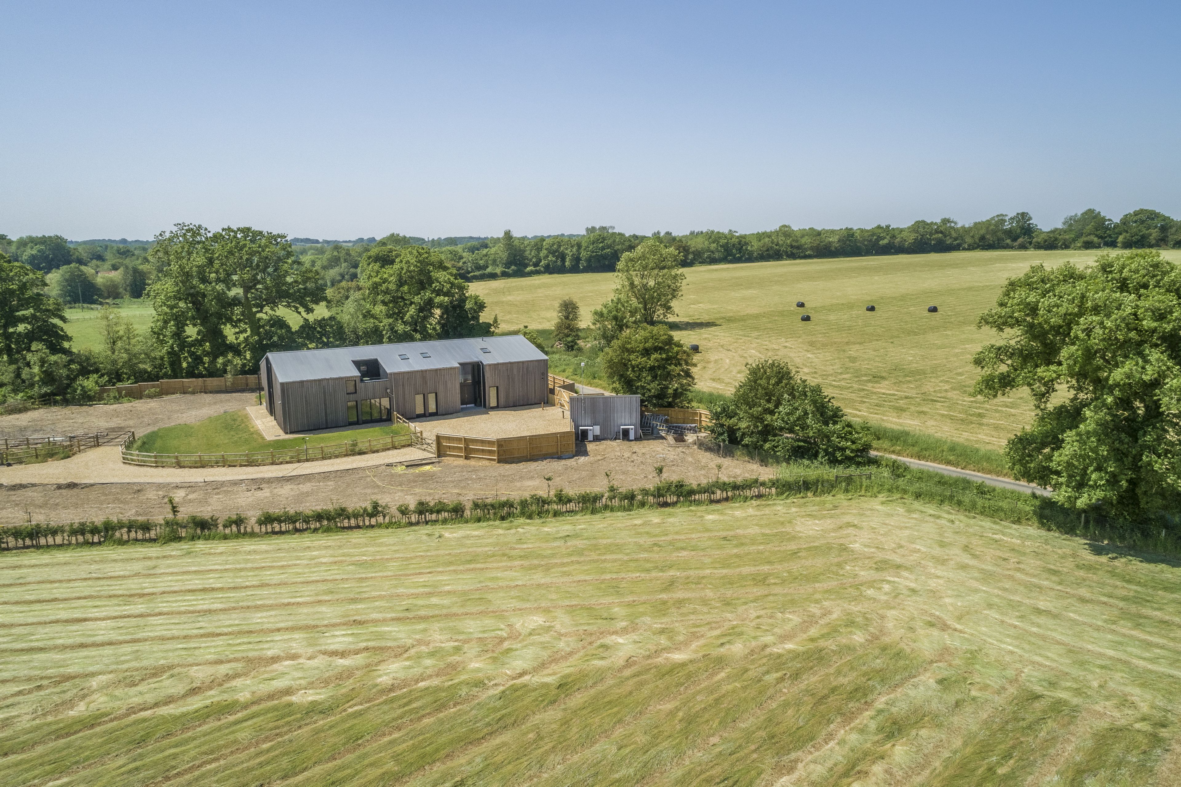 A modern farmhouse with a large barn, surrounded by expansive fields and trees.