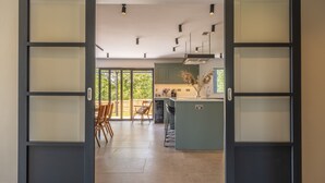 A modern kitchen with a central island, green cabinets, and a dining area with chairs. - The Grain Store, Reepham, Norfolk (Reepham)