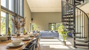 A modern dining area with a wooden table set for a meal, a blue sofa in the background, and a spiral staircase. - The Grain Store, Reepham, Norfolk (Reepham)