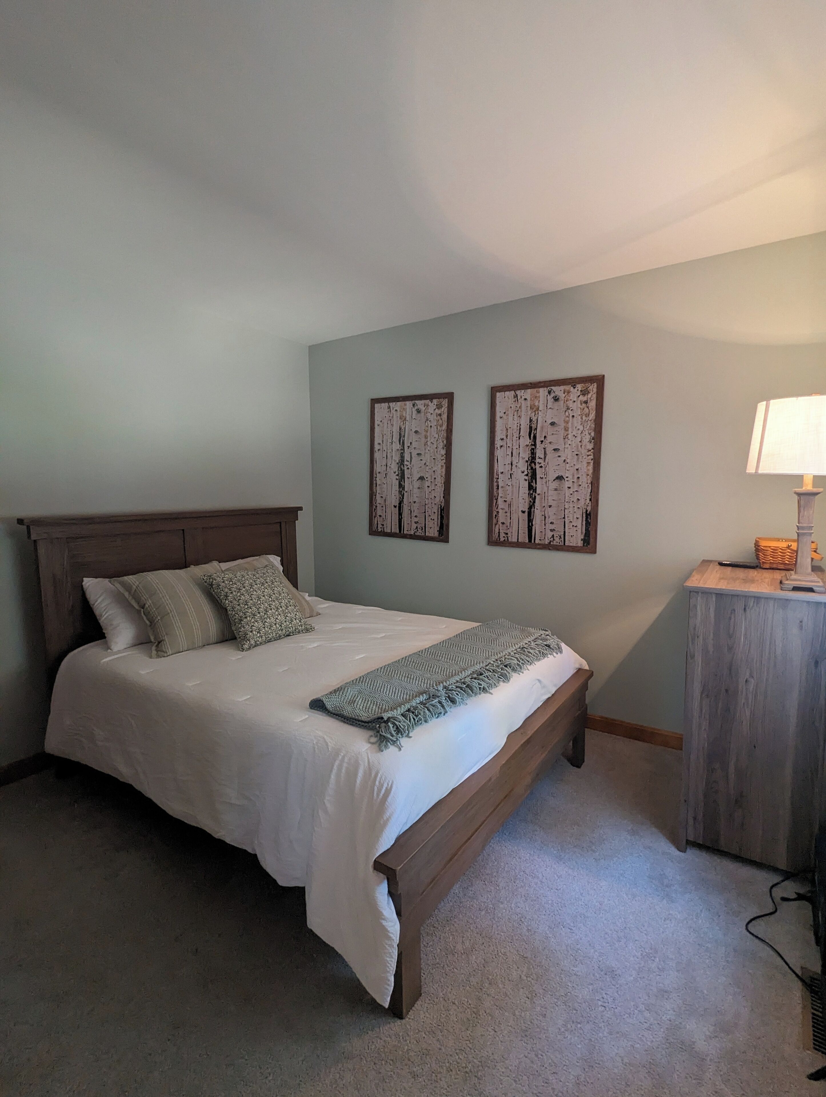 Un dormitorio con una cama de madera, una mesita de noche y dos cuadros en la pared.