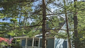 Une maison de plain-pied avec un porche, entourée d’arbres et surmontée d’un drapeau.