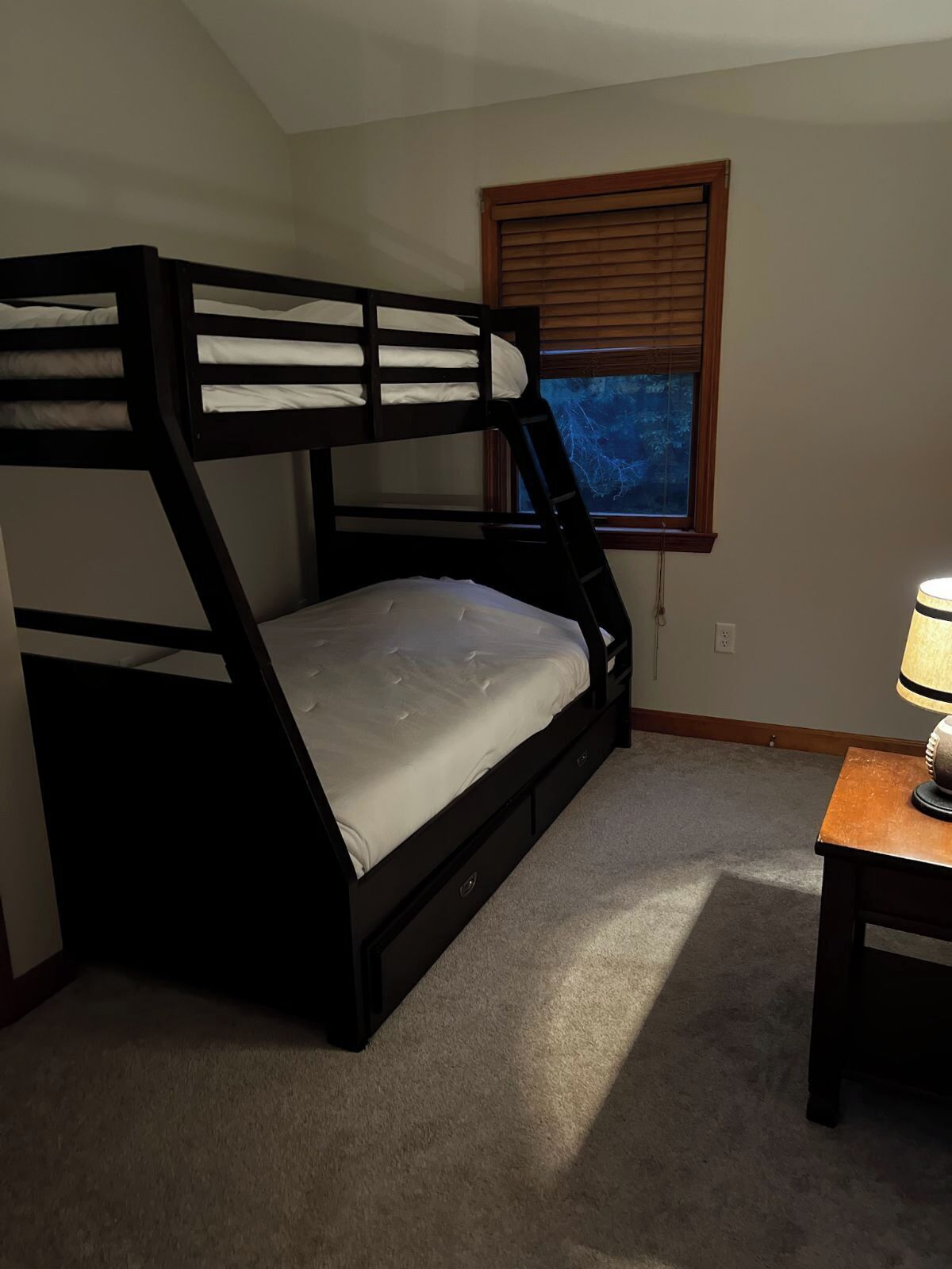 A bunk bed in a room with a window and a lamp on a side table.