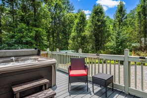 A hot tub on a wooden deck with a chair and table, surrounded by a wooden railing and a forested area. - Romantic hot tub cabin | Secluded (Cosby)