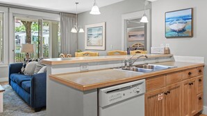 A modern kitchen with a built-in dishwasher, wooden cabinets, and a large window overlooking a balcony. - Poolside 2BR Condo at Baytowne Wharf! GOLF CART to Beach, Pool, Hot Tub, Tram (Miramar Beach)