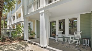 A multi-story building with a covered porch, outdoor seating, and a white picket fence. - Poolside 2BR Condo at Baytowne Wharf! GOLF CART to Beach, Pool, Hot Tub, Tram (Miramar Beach)