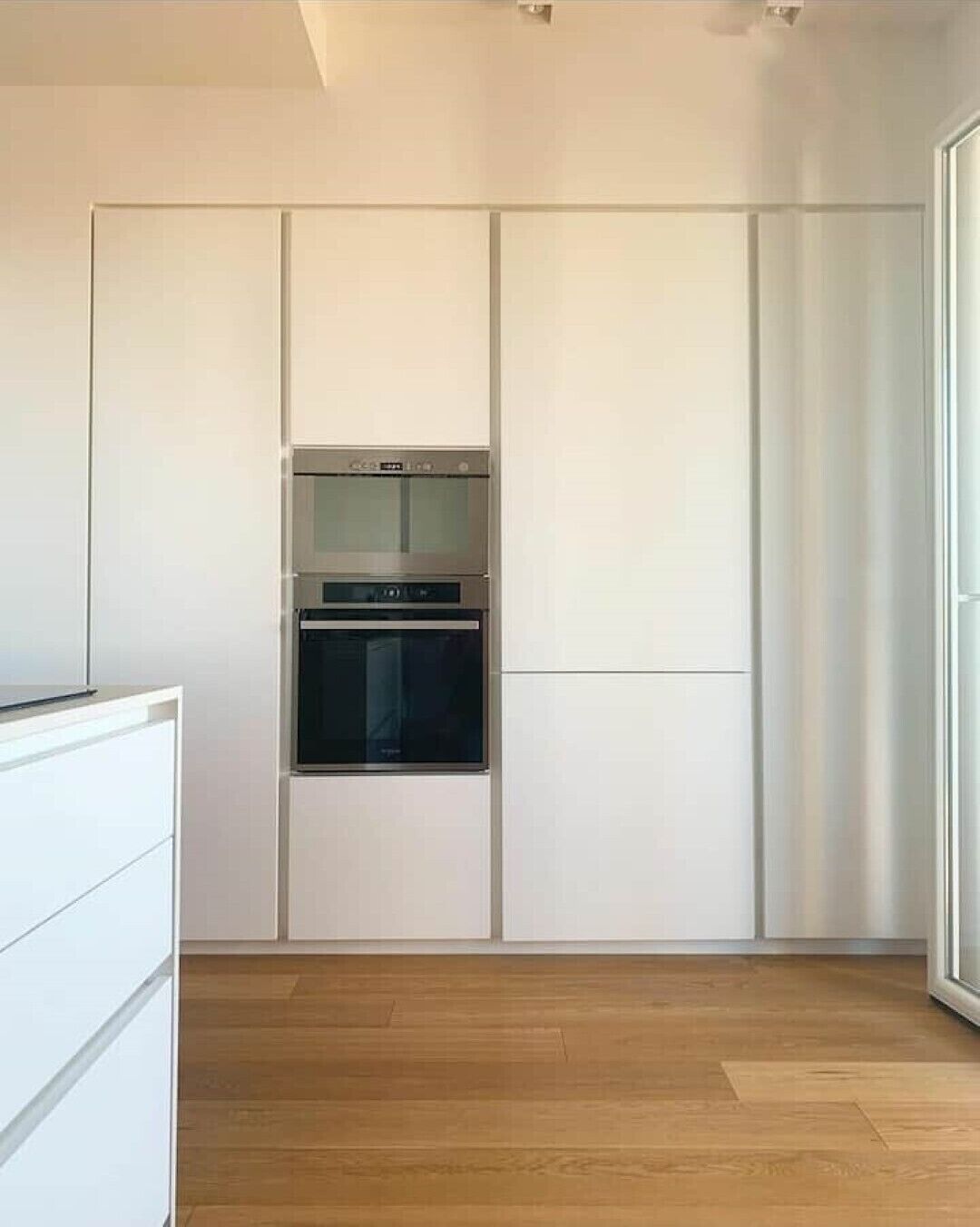 Een moderne keuken met inbouwapparatuur, witte kasten en een houten vloer.
