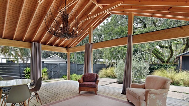 Un patio cubierto al aire libre con suelo de madera, dos sillones, una mesa de comedor con sillas y un tapete grande.