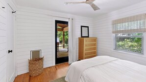 Un dormitorio con cama, cómoda de madera, cesta de mimbre y ventana con persianas.