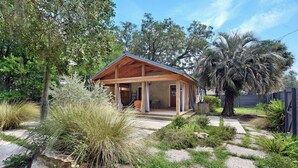 Una cabaña de madera con un porche, rodeada de plantas y árboles.