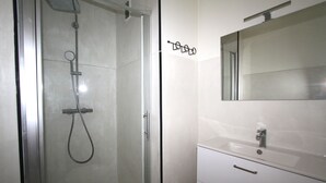 Ein modernes Badezimmer mit einer gläsernen Duschkabine, einem weißen Waschbecken mit Spiegel darüber und einem kleinen Handtuchhalter.