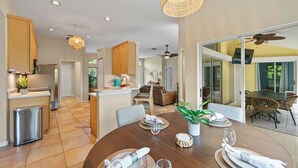 A modern kitchen with wooden cabinets, a dining area with a round table set for four, and a view of the outdoor patio. - Shared Dock and Private Backyard with Pool -Casa Mango (Sarasota)