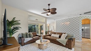 A modern living room with a brown leather sofa, a wooden coffee table, and a ceiling fan. - Shared Dock and Private Backyard with Pool -Casa Mango (Sarasota)
