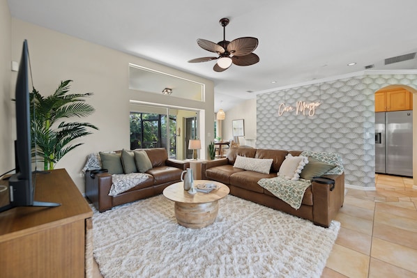 A modern living room with a brown leather sofa, a wooden coffee table, and a ceiling fan.
