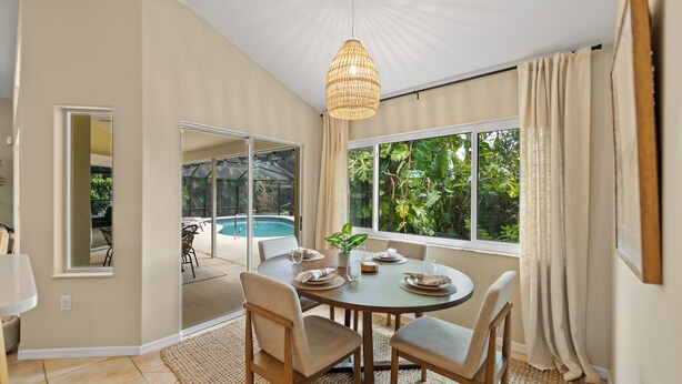 A dining area with a round table, chairs, and a hanging light fixture. There is a view of a swimming pool through a glass door. - Shared Dock and Private Backyard with Pool -Casa Mango (Sarasota)