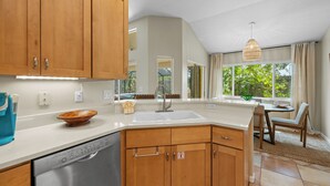 A kitchen with wooden cabinets, a dishwasher, a sink, and a dining area with a table and chairs. - Shared Dock and Private Backyard with Pool -Casa Mango (Sarasota)
