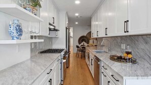 A modern kitchen with white cabinetry, marble countertops, and a central island with a sink and bar tools.