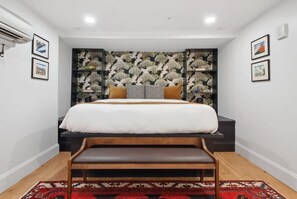 Un dormitorio con cama, un banco, papel tapiz estampado y cuadros en las paredes.
