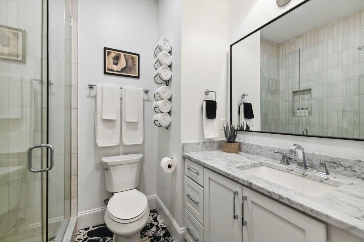 A modern bathroom with a glass shower enclosure, a toilet, a marble sink, and a large mirror.