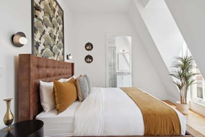 Un dormitorio moderno con una cama grande, cabecera de madera y vista a un baño a través de una puerta de cristal.