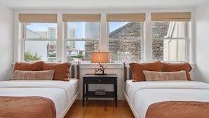 A bedroom with two beds, a nightstand, and a window with a view of buildings.