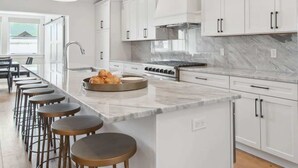 A modern kitchen with white cabinets, a marble countertop, and a central island with bar stools.