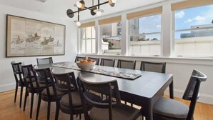 A dining area with a large table, chairs, a chandelier, and a painting on the wall.