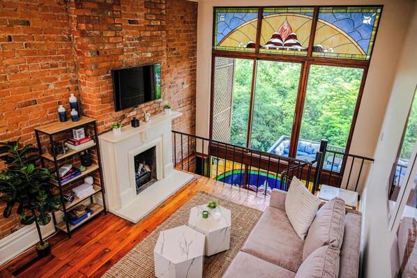 Una sala de estar con pared de ladrillo, chimenea, ventana grande con vistas a vegetación y sofá moderno.