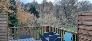 A wooden deck with two chairs and a table, surrounded by autumn foliage and trees.