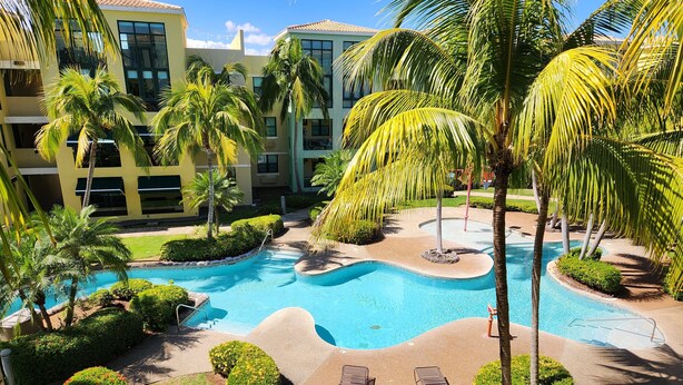 A resort with a swimming pool, palm trees, and a building with multiple floors. - Aquatika Minimalist Beach Escape (Loiza)