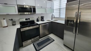 A modern kitchen with stainless steel appliances, white cabinetry, and a black countertop. - Aquatika Minimalist Beach Escape (Loiza)