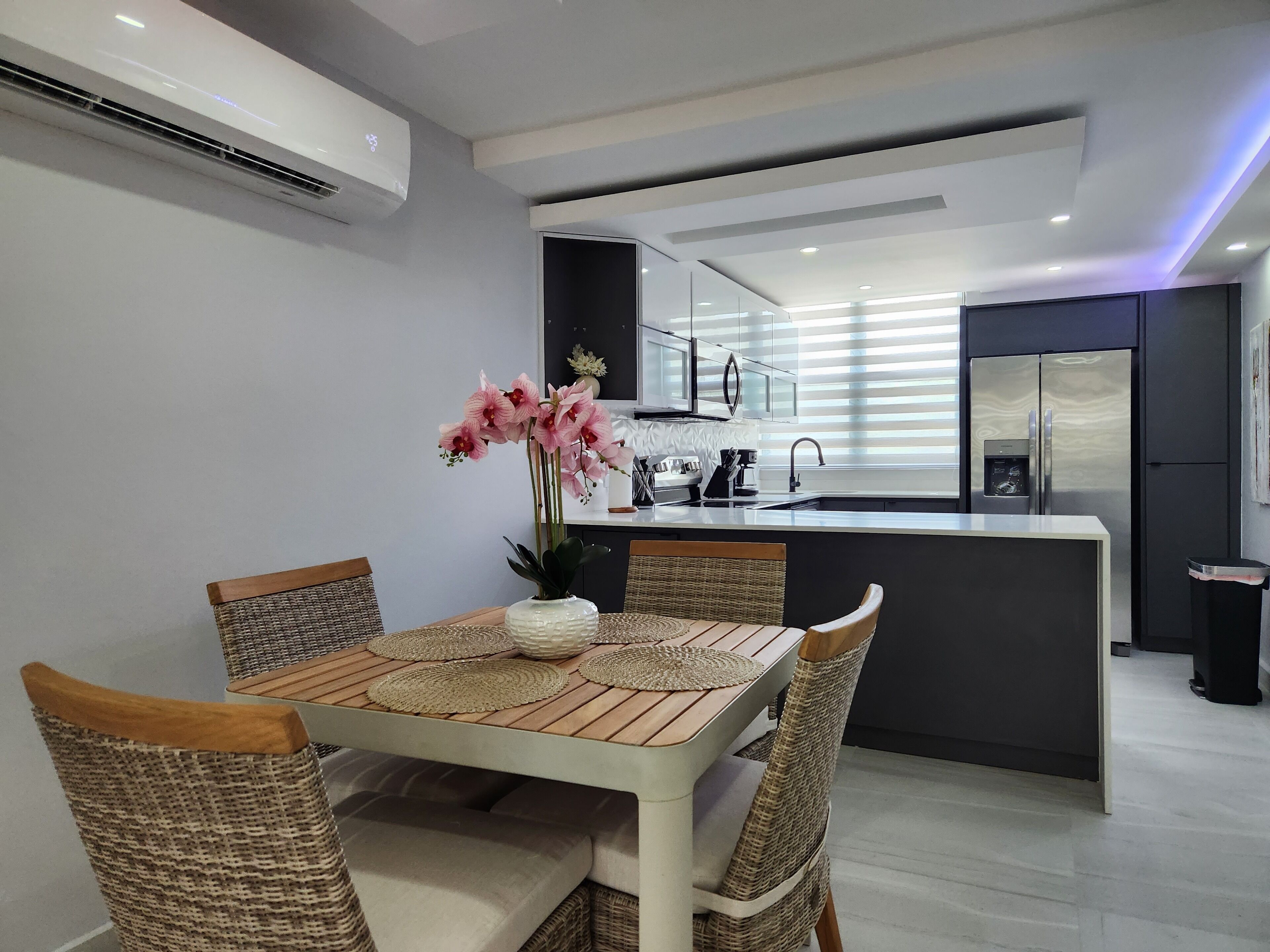 Una cocina moderna con una isla central, muebles blancos y un refrigerador de acero inoxidable.