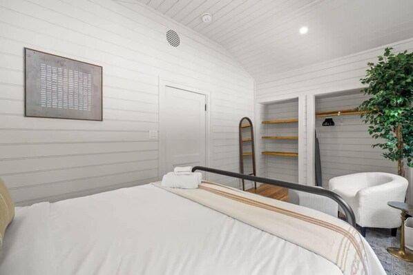 Ein Hotelzimmer mit Bett, Sessel, Pflanze und Kleiderschrank.