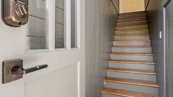 A narrow stairway with a metal handrail and a black mat at the bottom.