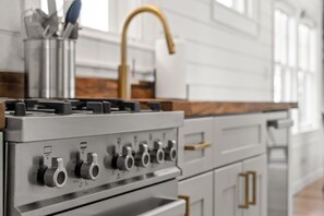 A kitchen with a stainless steel range hood, a gold faucet, and a white cabinet with gold handles.