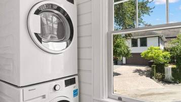 A stacked washer and dryer unit in a room with white paneled walls and a window overlooking a driveway.